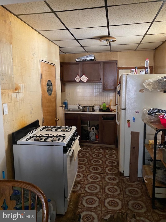 kitchen with decorative backsplash, a drop ceiling, range with gas stovetop, white fridge, and dark tile patterned flooring