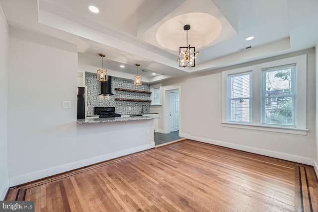 kitchen with kitchen peninsula, stainless steel refrigerator, hardwood / wood-style flooring, and a raised ceiling