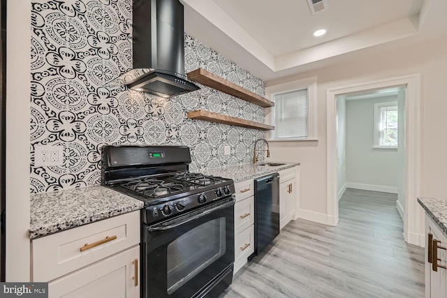 kitchen with wall chimney exhaust hood, white cabinetry, black appliances, and light stone counters