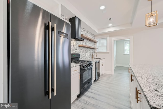 kitchen featuring white cabinets, wall chimney exhaust hood, decorative light fixtures, and appliances with stainless steel finishes