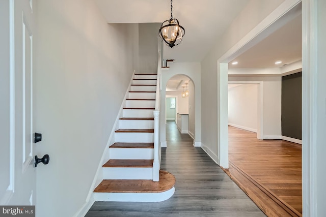 stairway with wood-type flooring and an inviting chandelier