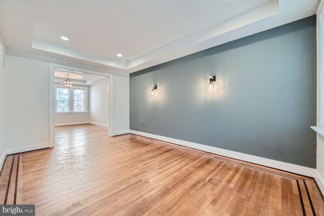 unfurnished room with light hardwood / wood-style floors, a raised ceiling, and a notable chandelier