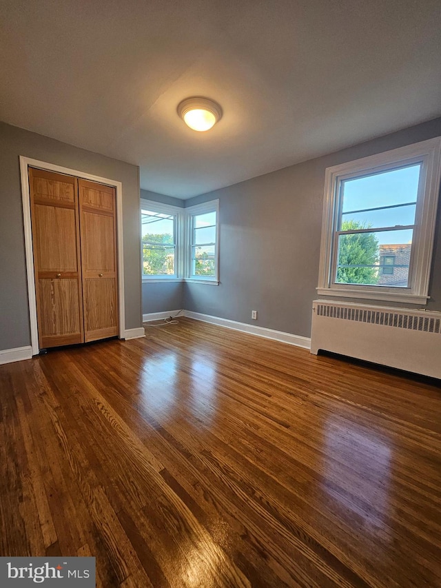 unfurnished bedroom featuring radiator heating unit, dark hardwood / wood-style flooring, and a closet