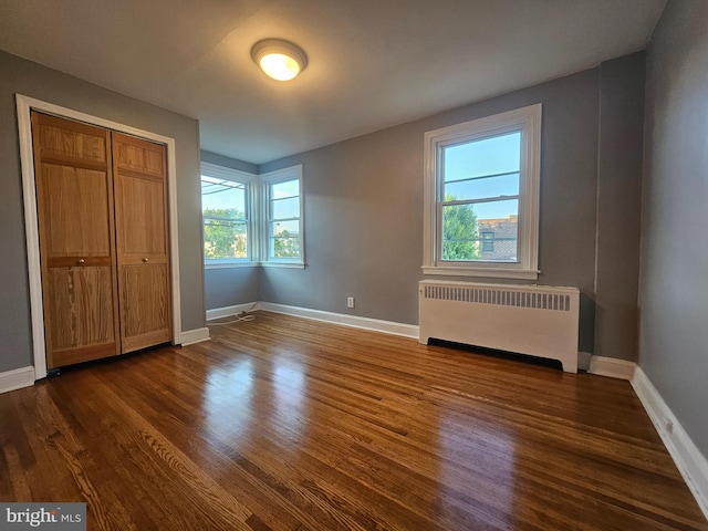 unfurnished bedroom with radiator, multiple windows, and dark hardwood / wood-style floors