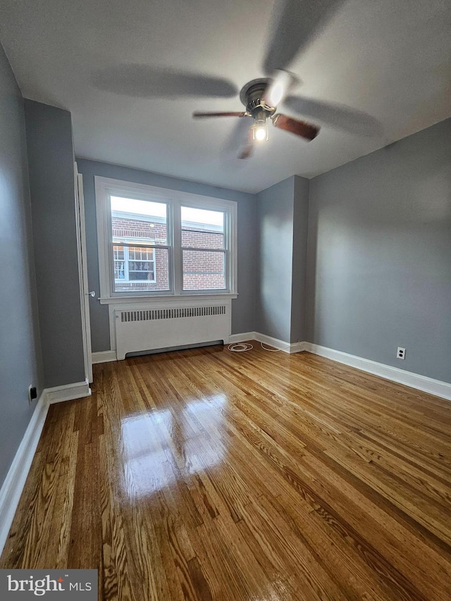 spare room with radiator, ceiling fan, and wood-type flooring