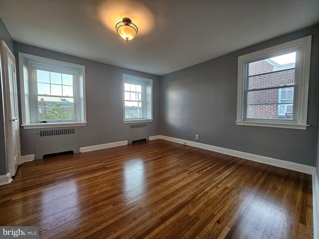 unfurnished room featuring radiator heating unit and dark hardwood / wood-style floors