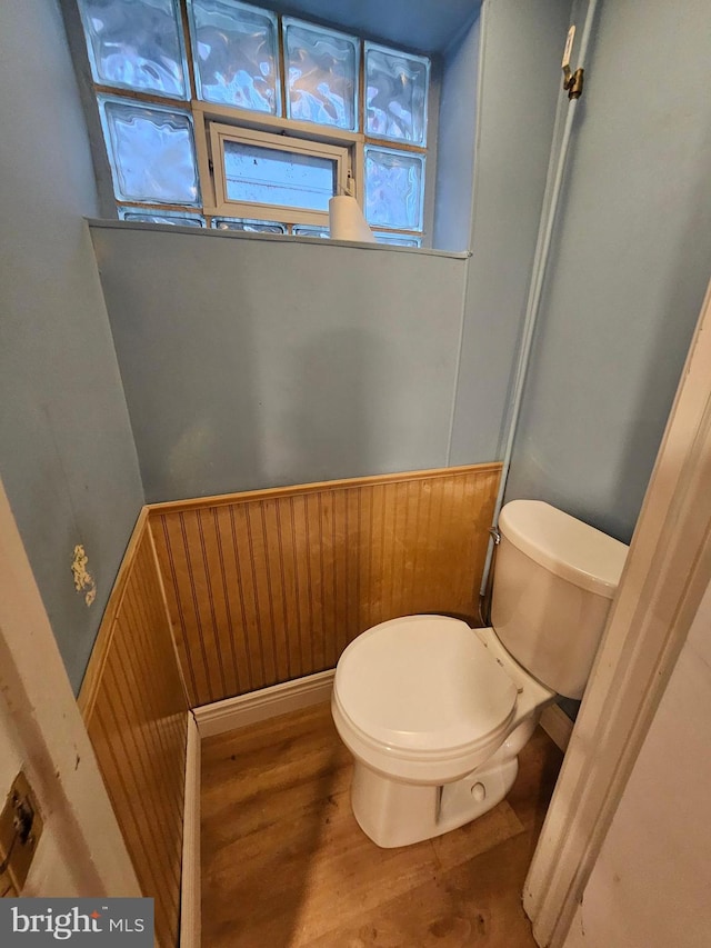 bathroom with wood-type flooring, wooden walls, and toilet