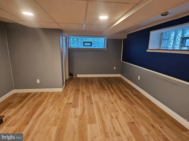 basement with a wealth of natural light, light wood-type flooring, and a paneled ceiling