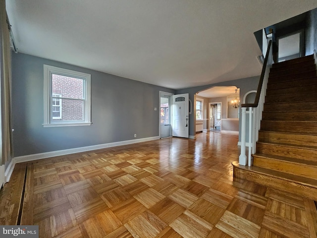 unfurnished living room with a healthy amount of sunlight, a chandelier, and parquet floors