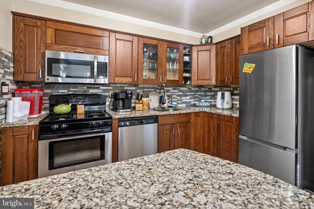 kitchen featuring backsplash, stainless steel appliances, and light stone counters