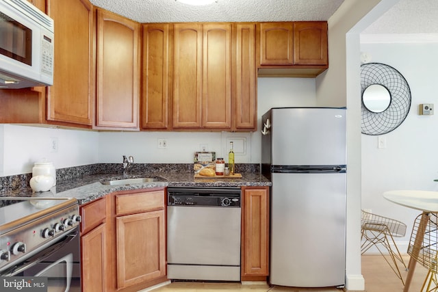 kitchen featuring appliances with stainless steel finishes, sink, a textured ceiling, and dark stone counters