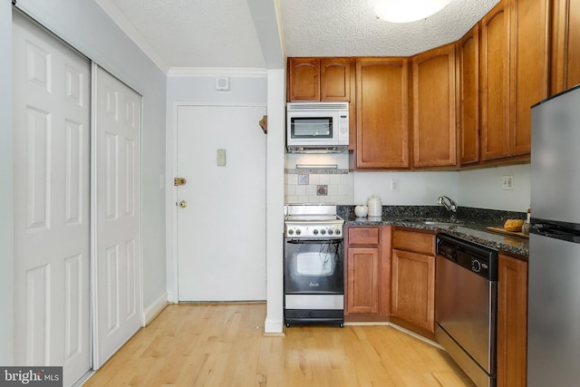 kitchen with appliances with stainless steel finishes, sink, dark stone countertops, light hardwood / wood-style floors, and a textured ceiling