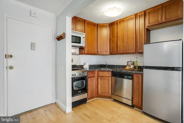 kitchen featuring appliances with stainless steel finishes, sink, a textured ceiling, and light hardwood / wood-style flooring