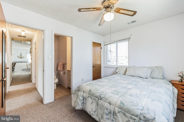 bedroom featuring ensuite bathroom, light carpet, and a textured ceiling