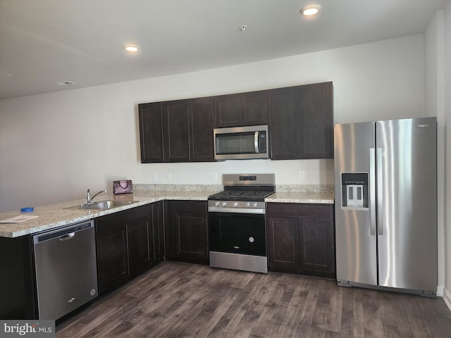 kitchen with kitchen peninsula, dark brown cabinets, dark wood-type flooring, stainless steel appliances, and sink