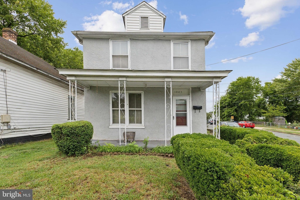 american foursquare style home featuring a porch, a front lawn, and stucco siding