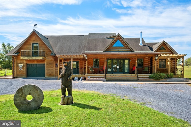 cabin with driveway, a front yard, a shingled roof, a garage, and a balcony