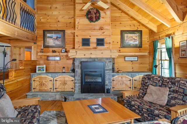 living area with beam ceiling, wooden walls, wooden ceiling, and a tiled fireplace