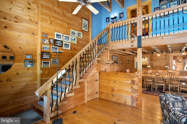 staircase featuring ceiling fan, a towering ceiling, hardwood / wood-style flooring, and wooden walls