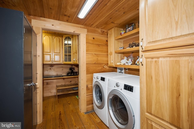 laundry area featuring hardwood / wood-style floors, wooden ceiling, cabinets, wooden walls, and washer and clothes dryer