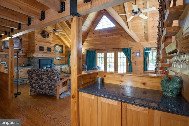 kitchen featuring ceiling fan, a stone fireplace, wood walls, hardwood / wood-style flooring, and vaulted ceiling with beams