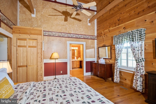 bedroom with ensuite bath, wooden walls, hardwood / wood-style floors, and ceiling fan