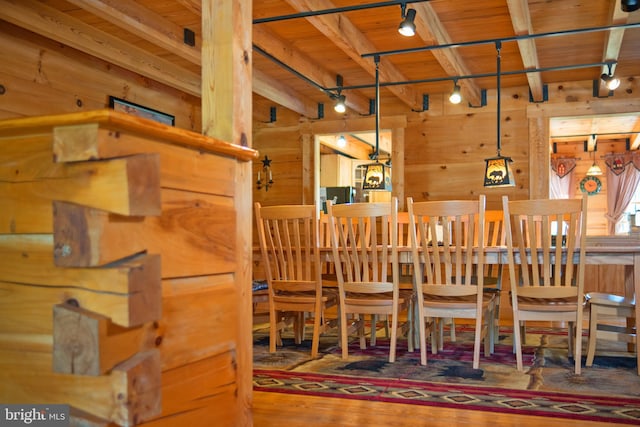 dining space with track lighting, wood walls, wood ceiling, beam ceiling, and wood finished floors