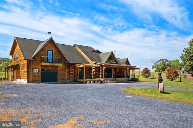 log cabin with a front yard, a balcony, gravel driveway, an attached garage, and covered porch