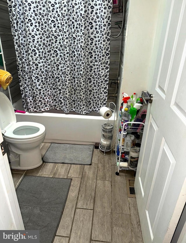 bathroom featuring wood-type flooring, toilet, and shower / tub combo