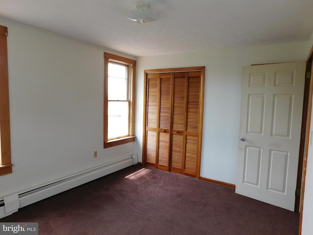 unfurnished bedroom featuring a baseboard heating unit, dark colored carpet, a closet, and baseboards