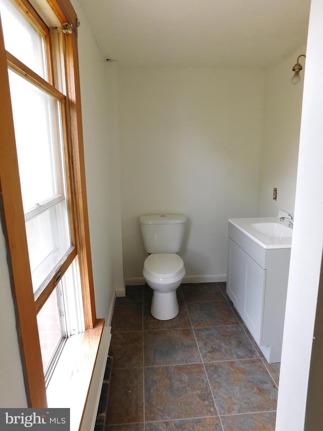 half bath featuring stone finish flooring, baseboards, vanity, and toilet