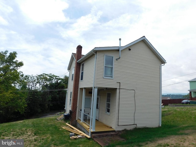 back of property with a chimney and a lawn