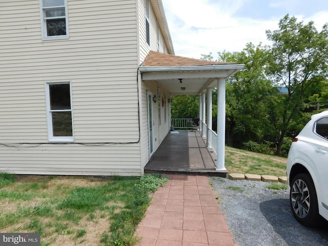 view of side of home featuring a shingled roof and covered porch