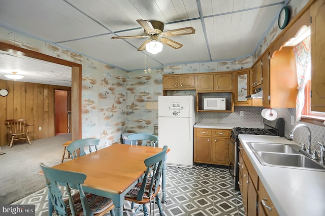 kitchen featuring sink, tasteful backsplash, white appliances, wooden walls, and ceiling fan