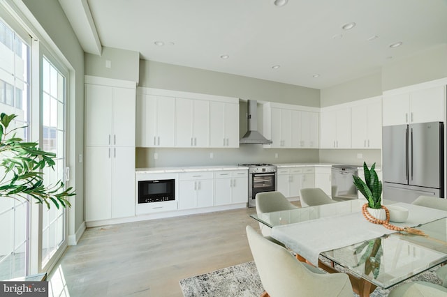 kitchen with appliances with stainless steel finishes, light countertops, wall chimney range hood, and white cabinetry