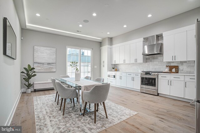 kitchen featuring light wood-type flooring, decorative backsplash, stainless steel range, white cabinetry, and wall chimney range hood