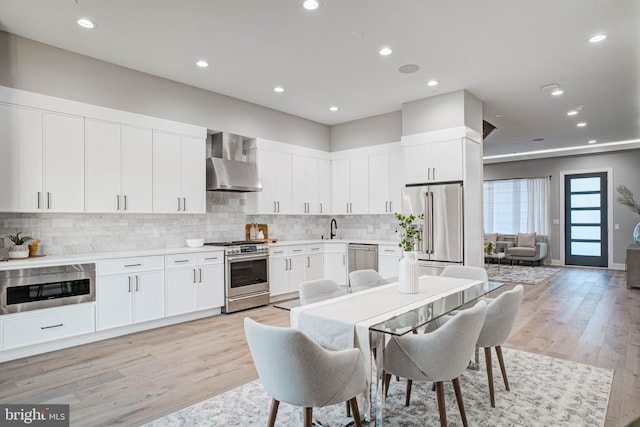 kitchen with premium appliances, a sink, white cabinets, light countertops, and wall chimney exhaust hood