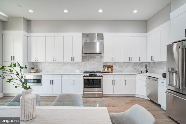 kitchen with light hardwood / wood-style flooring, backsplash, wall chimney exhaust hood, white cabinets, and stainless steel appliances