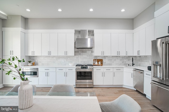 kitchen featuring stainless steel appliances, light countertops, white cabinets, a sink, and wall chimney exhaust hood