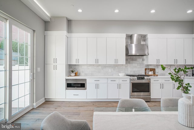 kitchen with white cabinets, light countertops, backsplash, wall chimney exhaust hood, and gas range