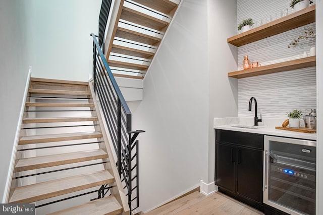 bar featuring wine cooler, stairway, a sink, light wood-style floors, and indoor wet bar