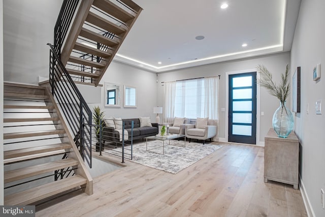 living room featuring light wood-type flooring, a raised ceiling, plenty of natural light, and stairway