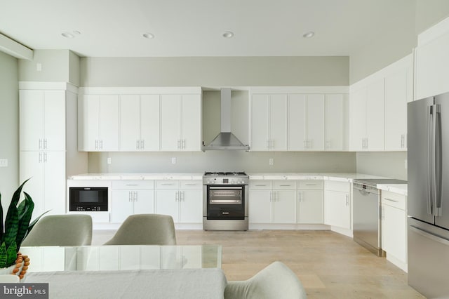 kitchen featuring light wood-style flooring, stainless steel appliances, white cabinetry, light countertops, and wall chimney range hood