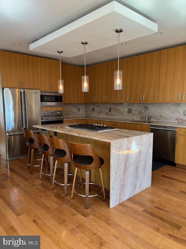 kitchen featuring decorative light fixtures, stainless steel appliances, light hardwood / wood-style floors, sink, and a kitchen island