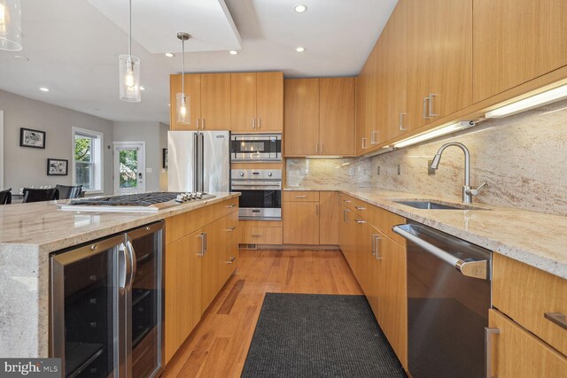 kitchen with light wood-type flooring, appliances with stainless steel finishes, light stone counters, sink, and pendant lighting