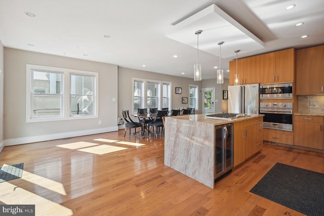 kitchen featuring light hardwood / wood-style flooring, light stone countertops, stainless steel appliances, beverage cooler, and a kitchen island