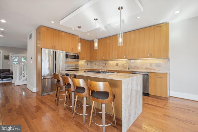 kitchen with light stone counters, a kitchen island, hanging light fixtures, appliances with stainless steel finishes, and light hardwood / wood-style floors