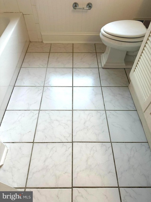 bathroom with a tub to relax in and toilet