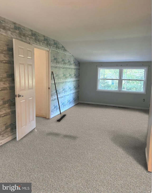 carpeted spare room featuring lofted ceiling and wood walls