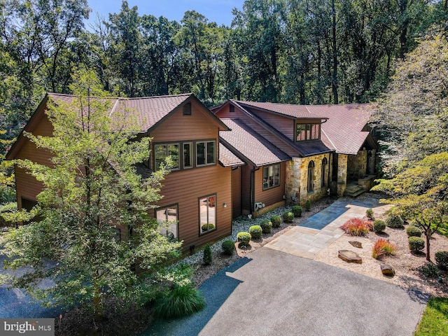 chalet / cabin featuring a forest view, stone siding, and driveway